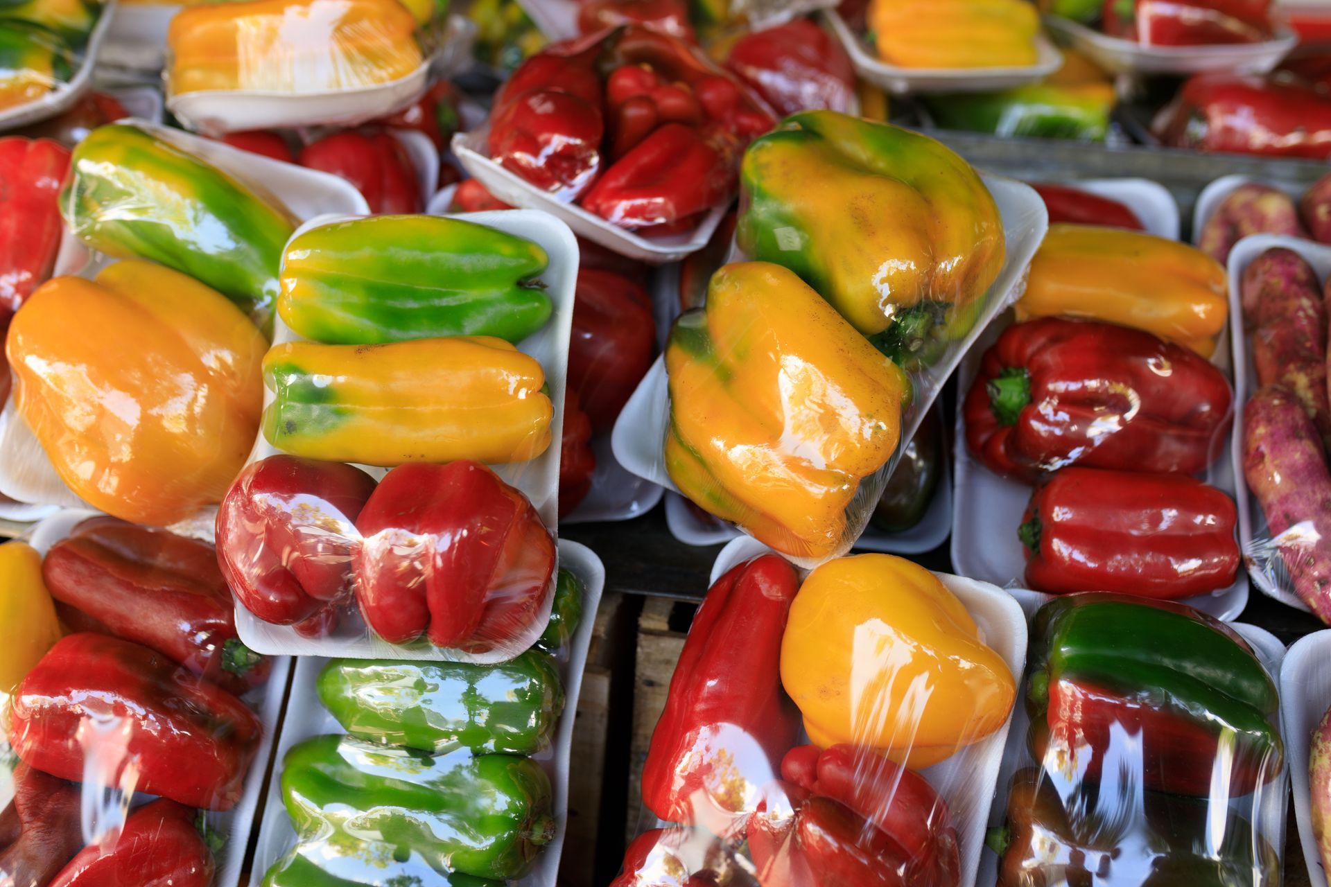 Vibrant assortment of packaged red, yellow, and green bell peppers at a market stall.